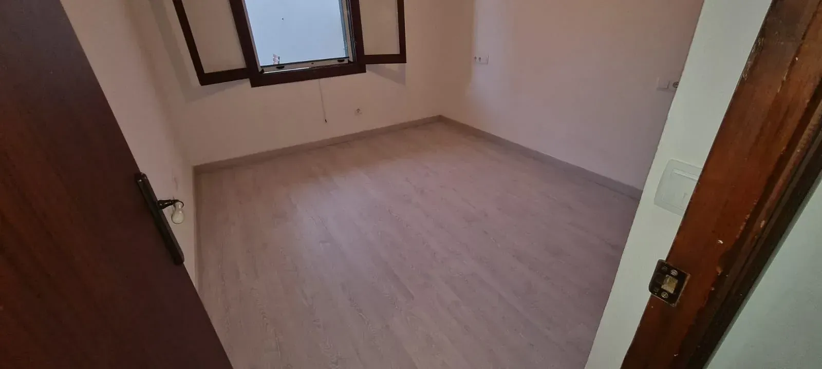 Una habitación vacía con suelo de madera y una ventana.
