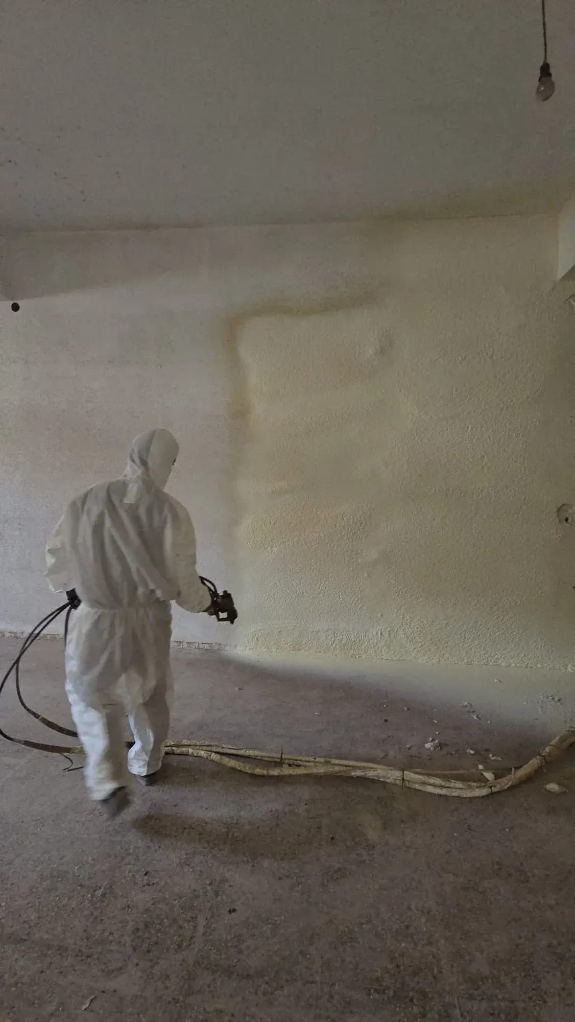 Un hombre con un traje de protección está rociando espuma sobre una pared.