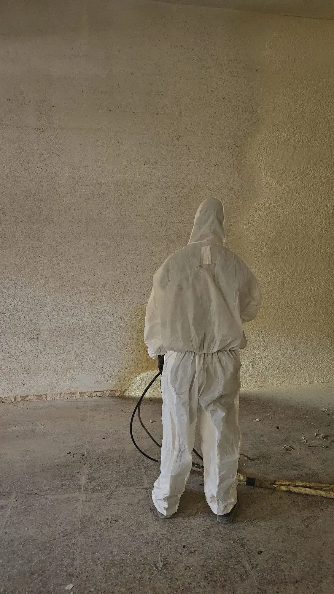 Un hombre con un traje de protección está rociando espuma sobre una pared.
