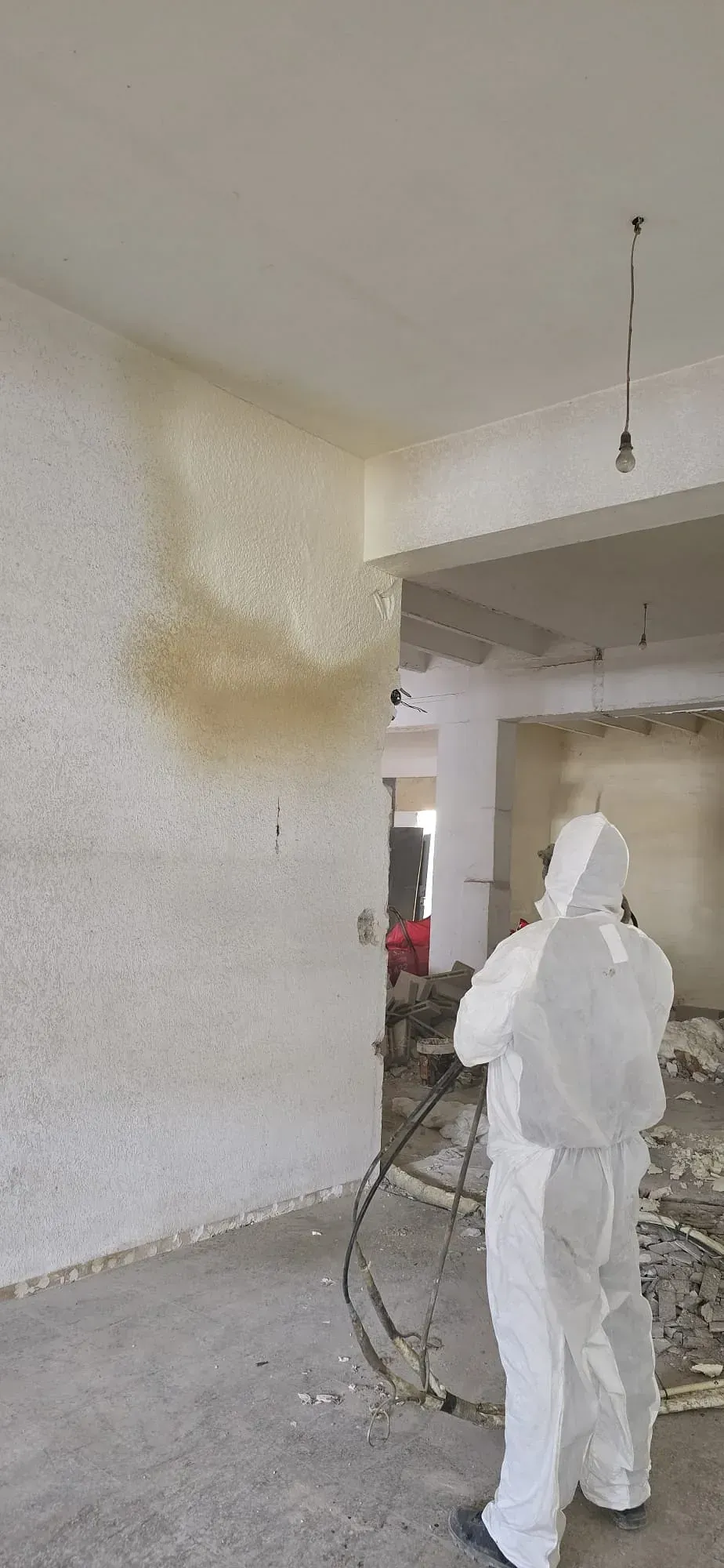 Un hombre con un traje de protección está rociando espuma sobre una pared.