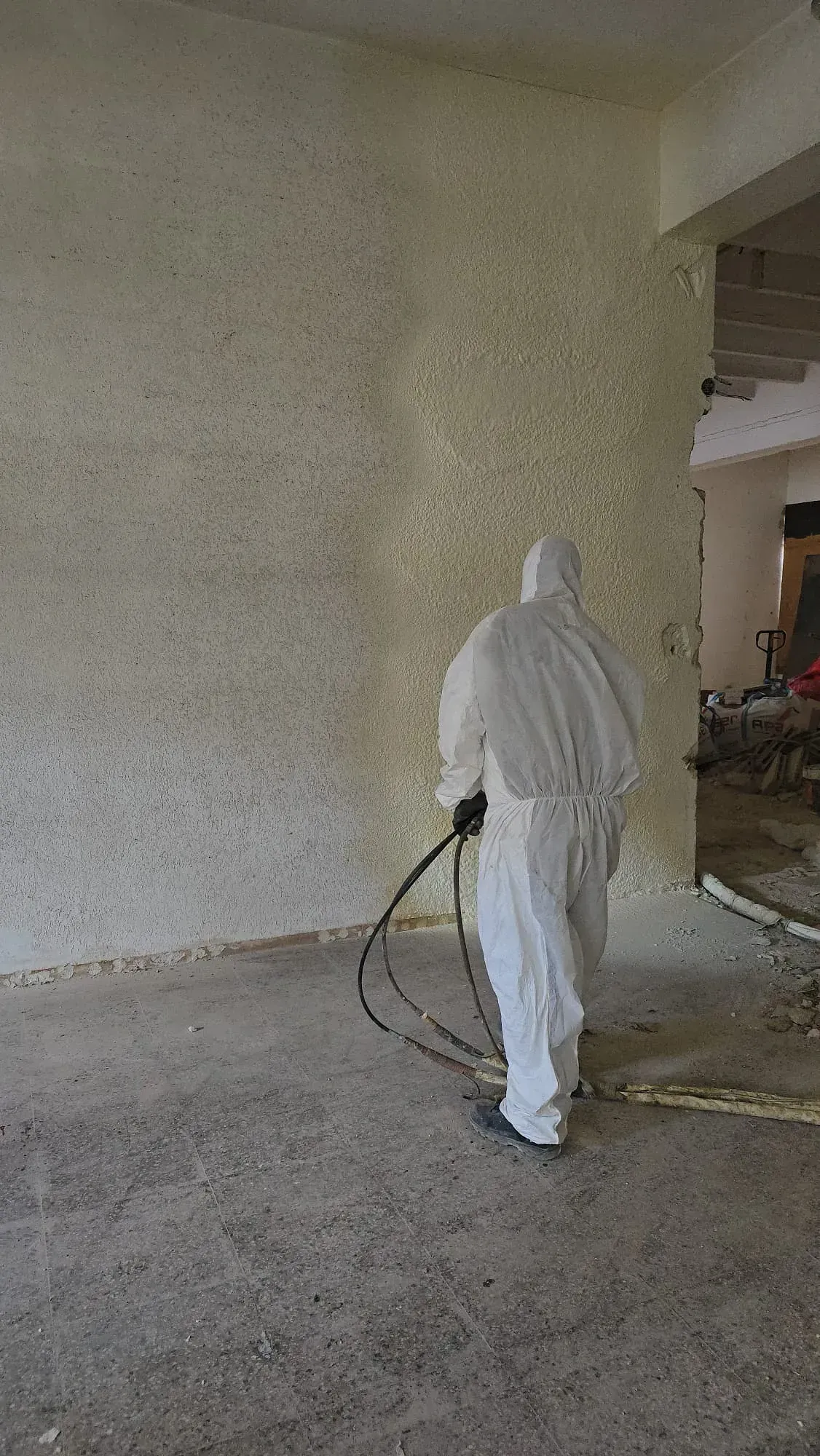 Un hombre con un traje de protección está rociando espuma sobre una pared.