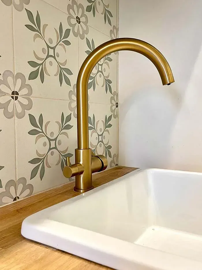 Un fregadero de cocina con grifo dorado y azulejos florales en la pared.