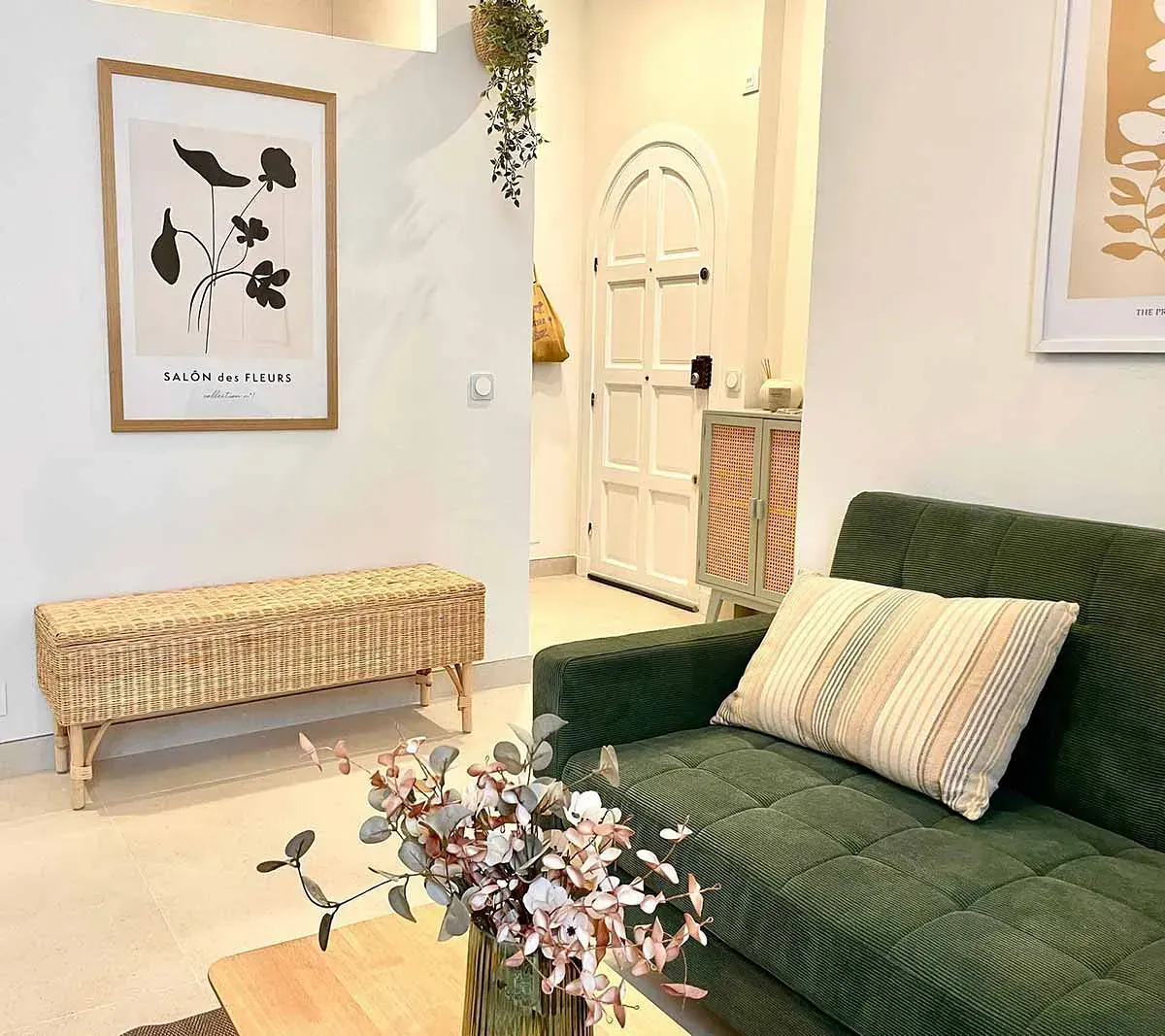 Una sala de estar con un sofá verde y un jarrón de flores sobre la mesa.