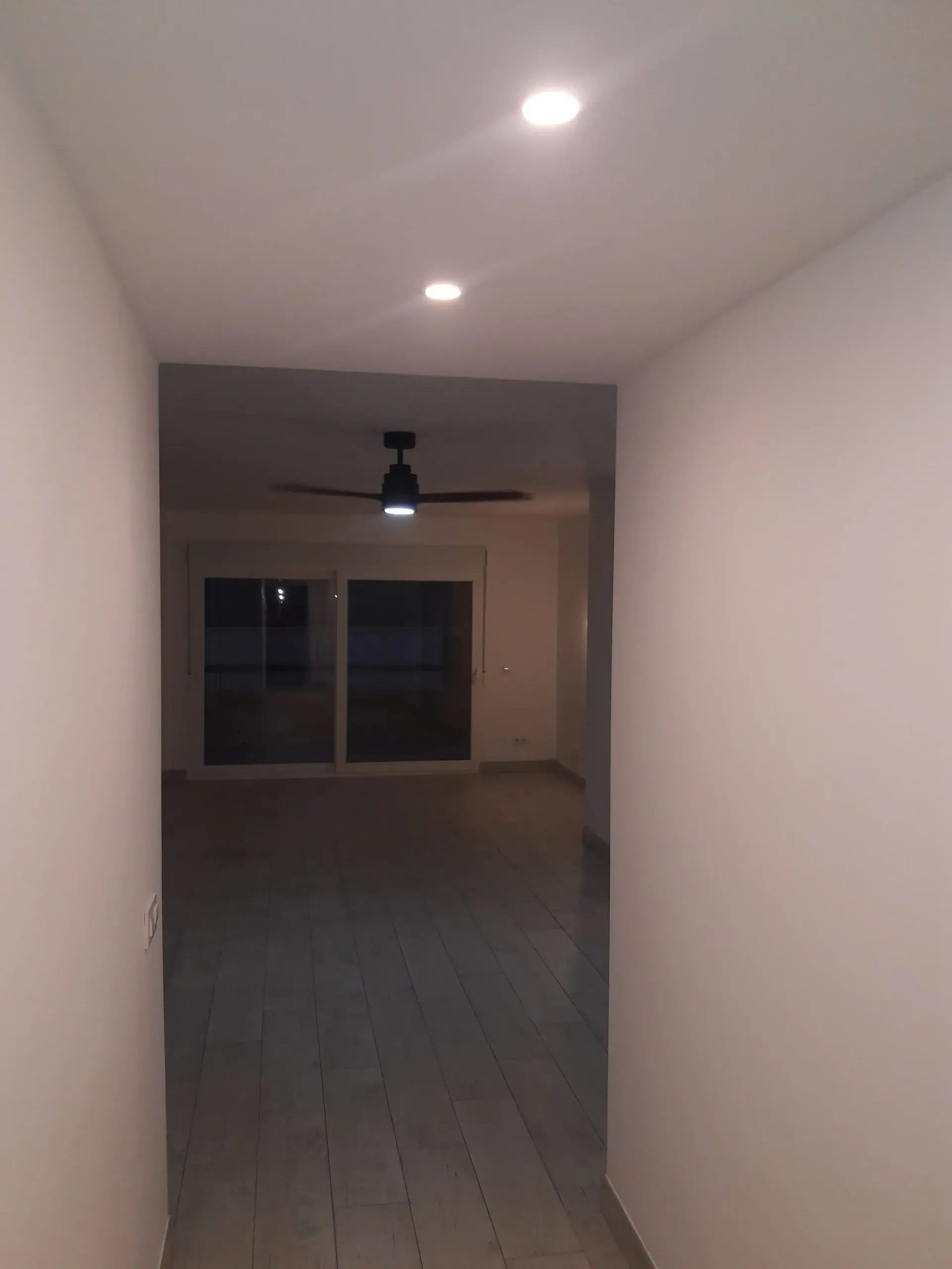 Un pasillo que conduce a una sala de estar con ventilador de techo y puertas corredizas de vidrio.