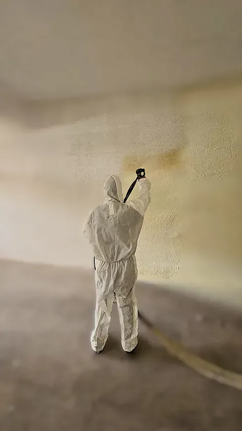 Un hombre con un traje de protección está rociando espuma sobre una pared.
