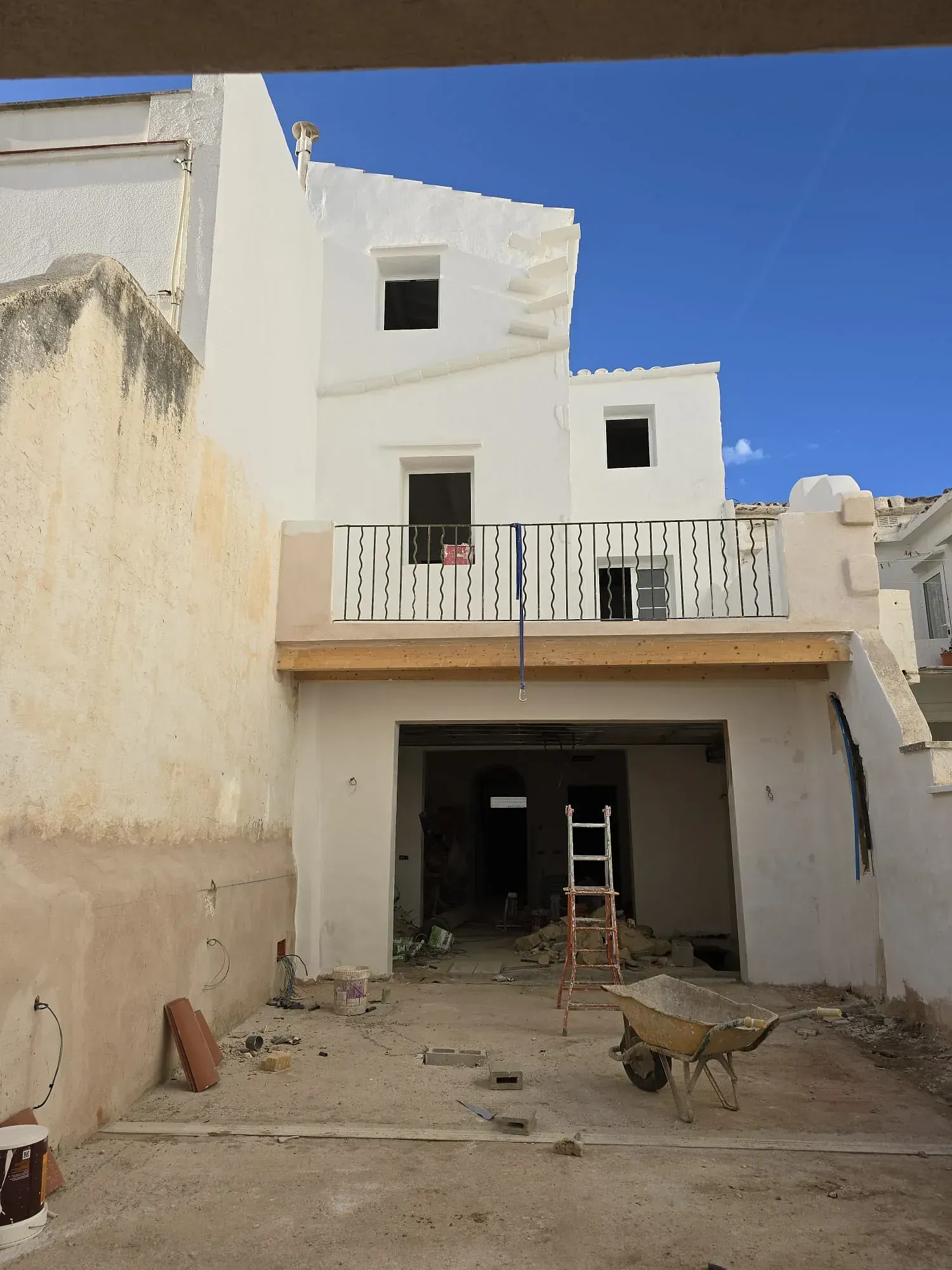 Un edificio blanco en construcción con una carretilla delante de él.