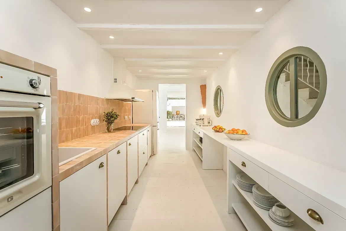 Una cocina con gabinetes blancos, una estufa y un espejo en la pared.