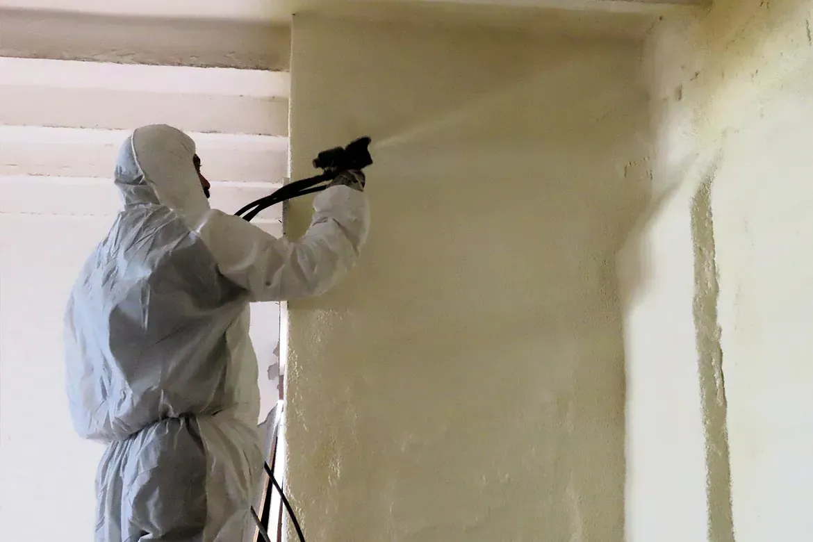 Un hombre con un traje de protección está rociando espuma sobre una pared.