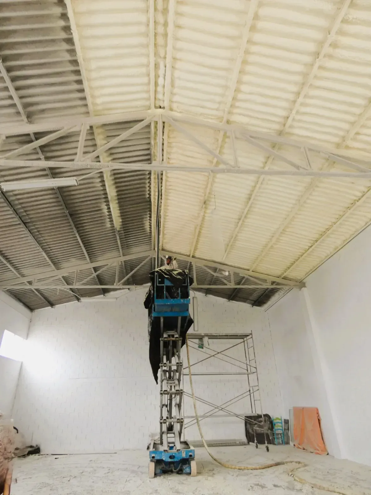 Un hombre está de pie sobre un elevador de tijera en un almacén vacío.