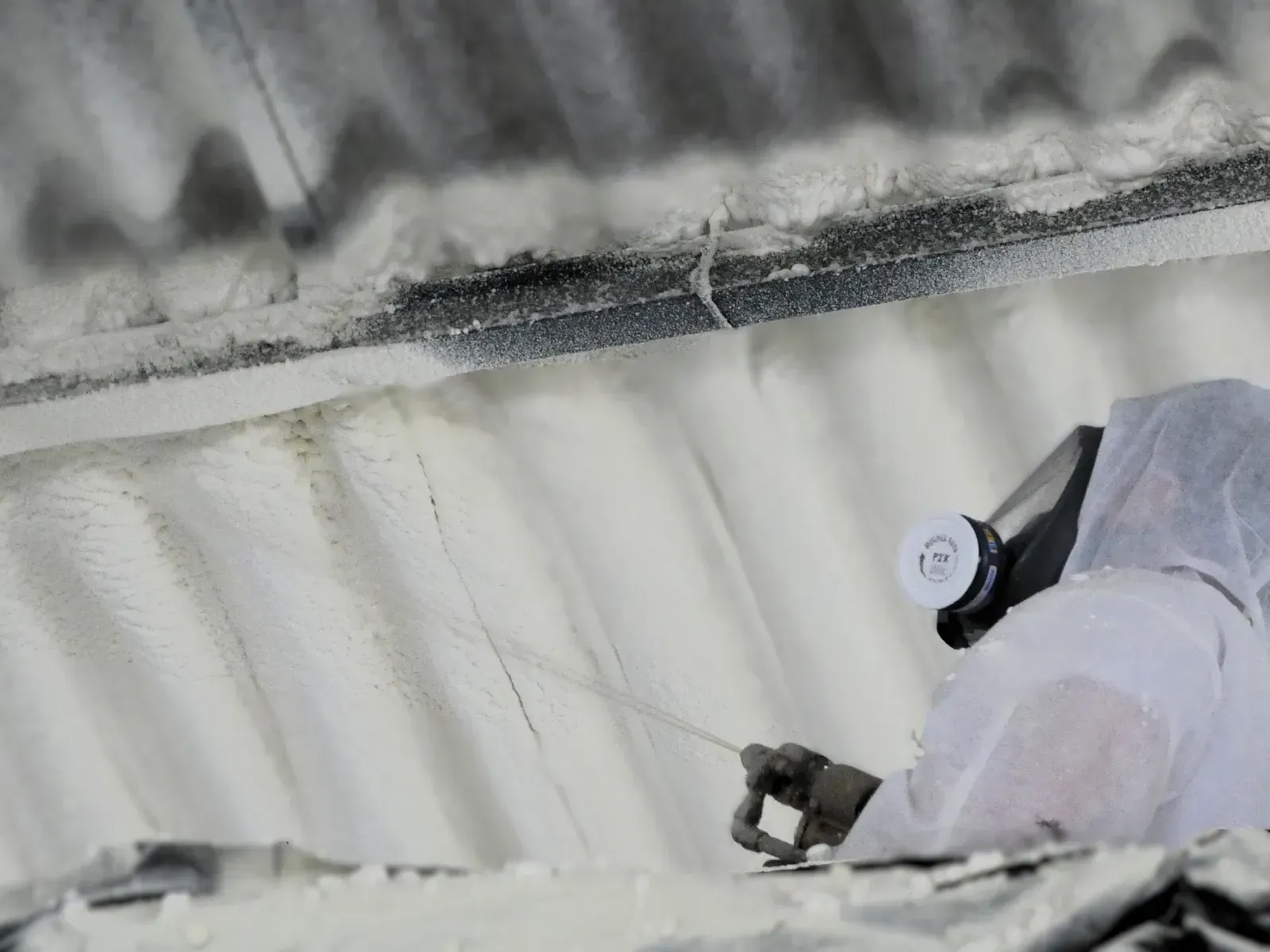 Un hombre que lleva una máscara de gas está rociando espuma sobre el techo de un edificio.
