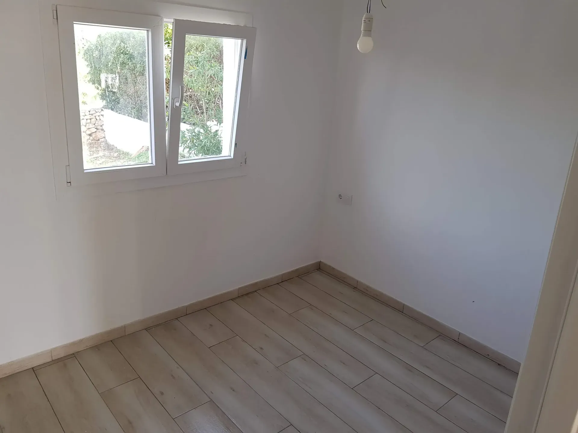 Una habitación vacía con suelo de madera y dos ventanas.