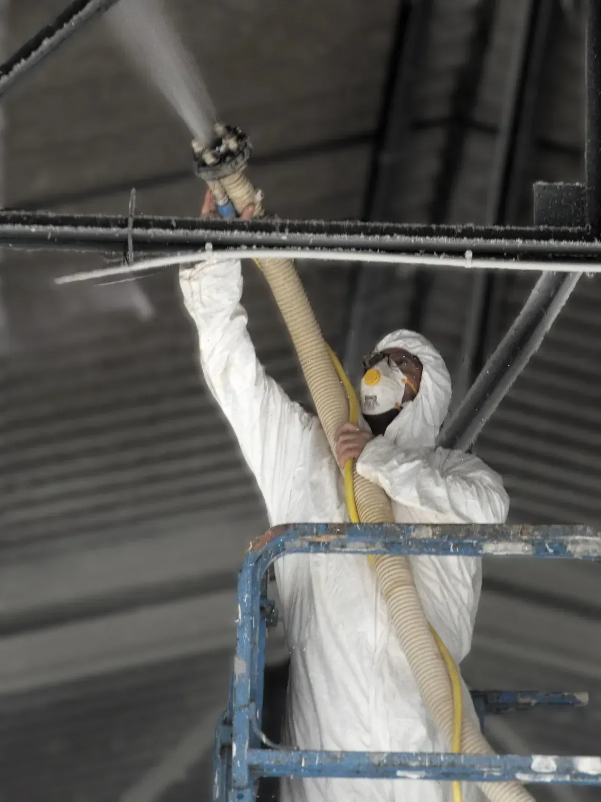 Un hombre con un traje de protección está rociando un techo con una manguera.