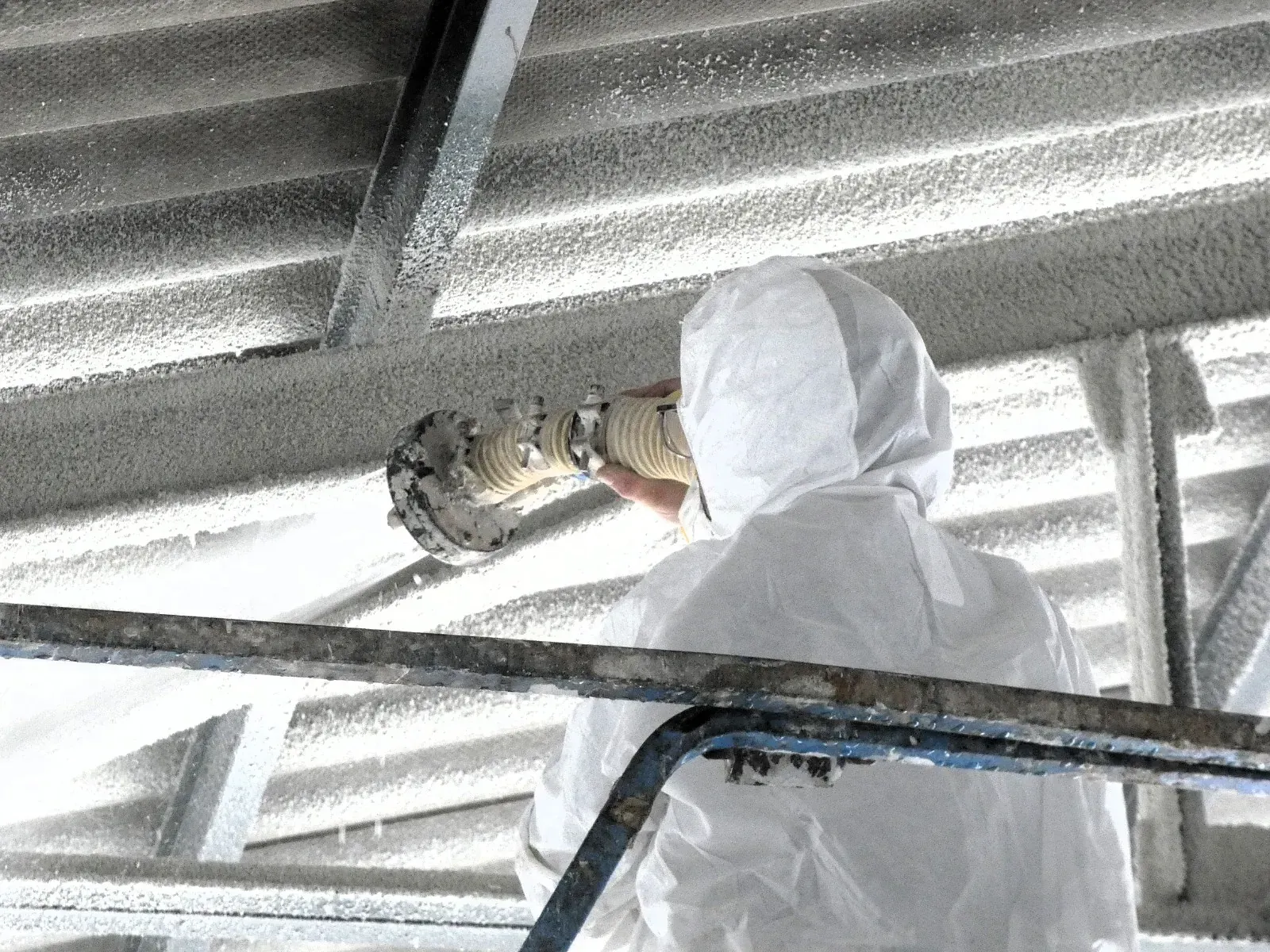 Un hombre con un traje de protección está rociando una tubería hacia el techo.