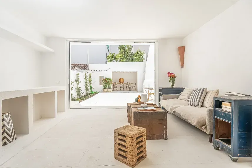 Una sala de estar con un sofá, una mesa, taburetes y una gran ventana.