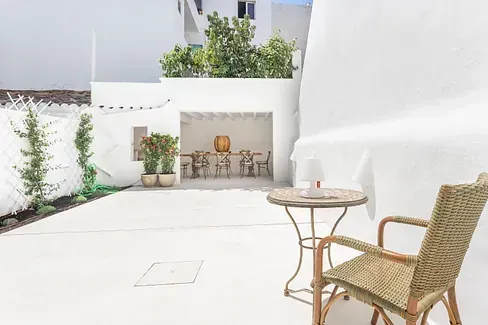 Un patio con una mesa y sillas frente a un edificio blanco.