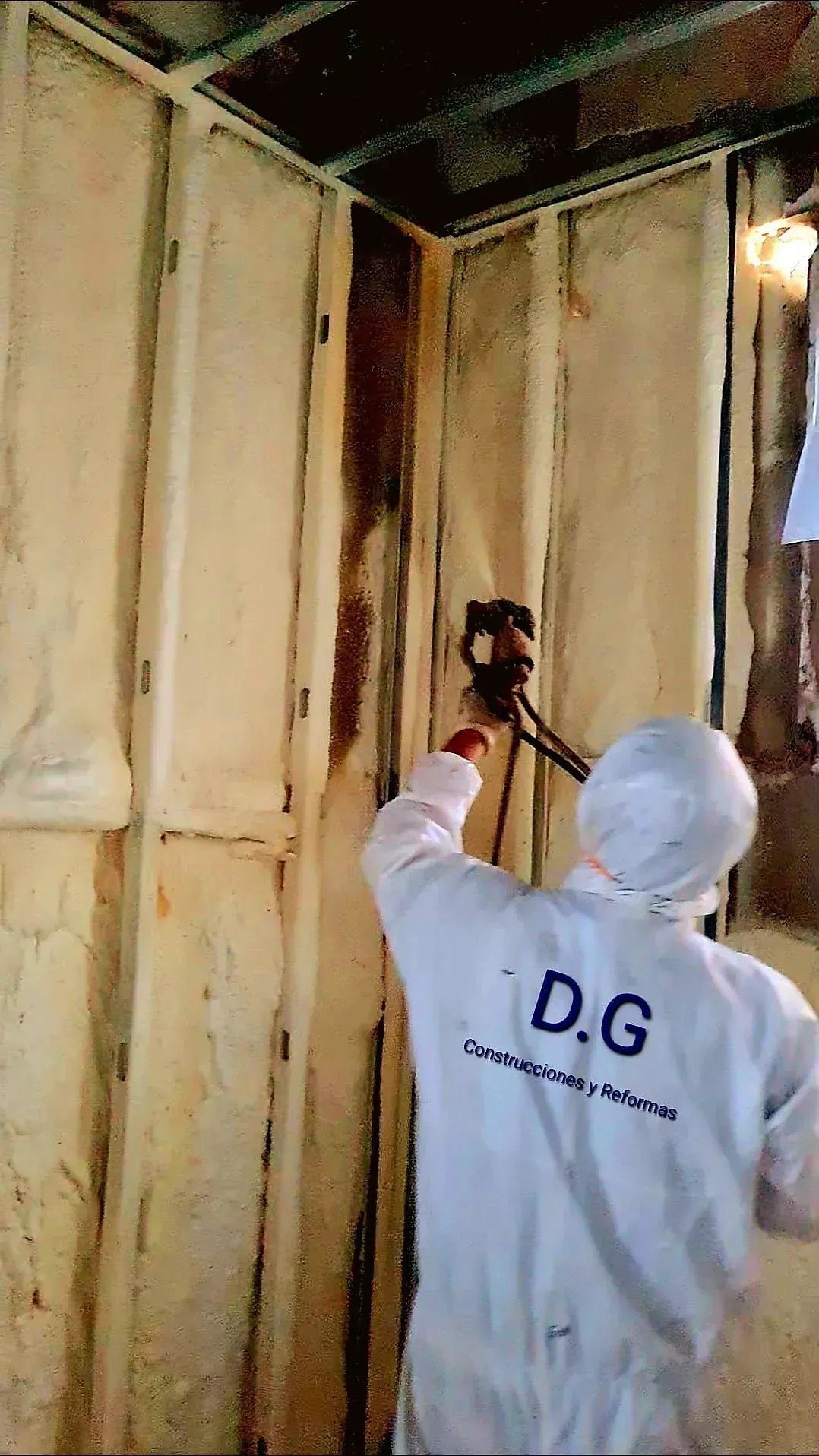 Un hombre con un traje blanco está rociando espuma en una pared.