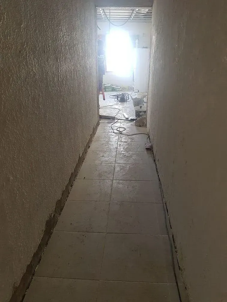 Un largo pasillo con suelo de baldosas y una pared blanca.
