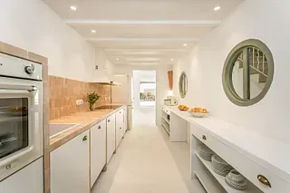 Una cocina con gabinetes blancos, una estufa, un fregadero y un espejo en la pared.