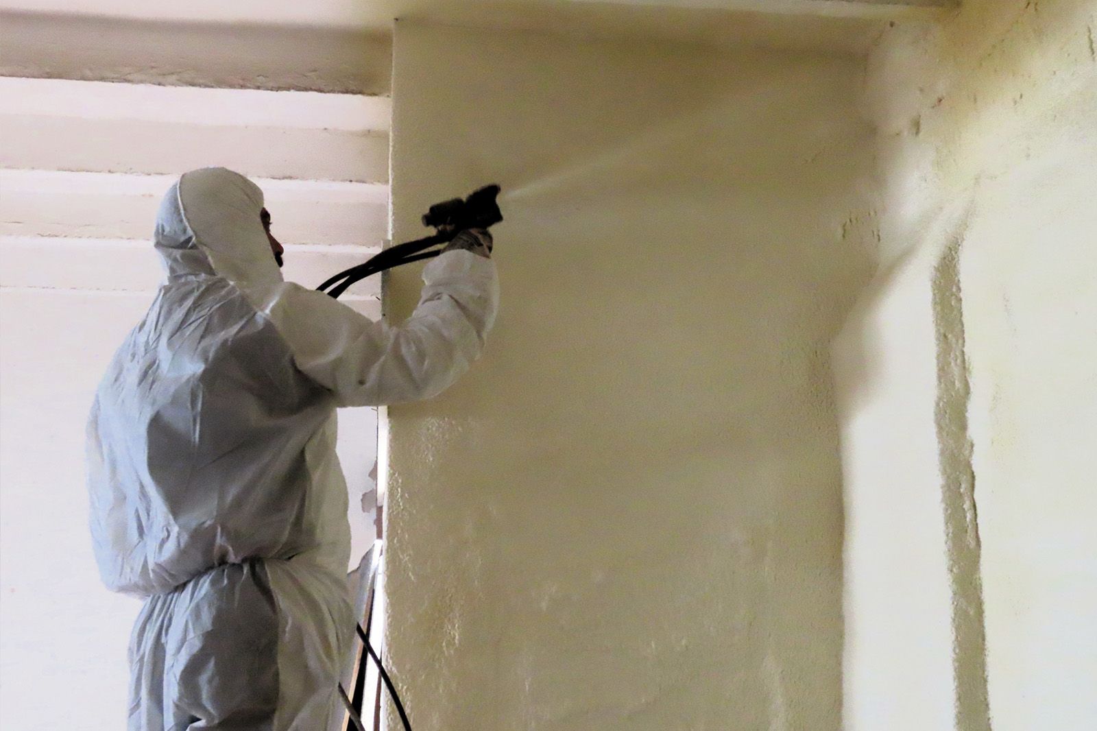 Un hombre con un traje de protección está rociando espuma sobre una pared.
