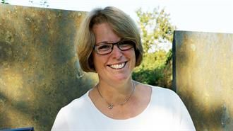 Eine Frau mit Brille und weißem Hemd lächelt in die Kamera.