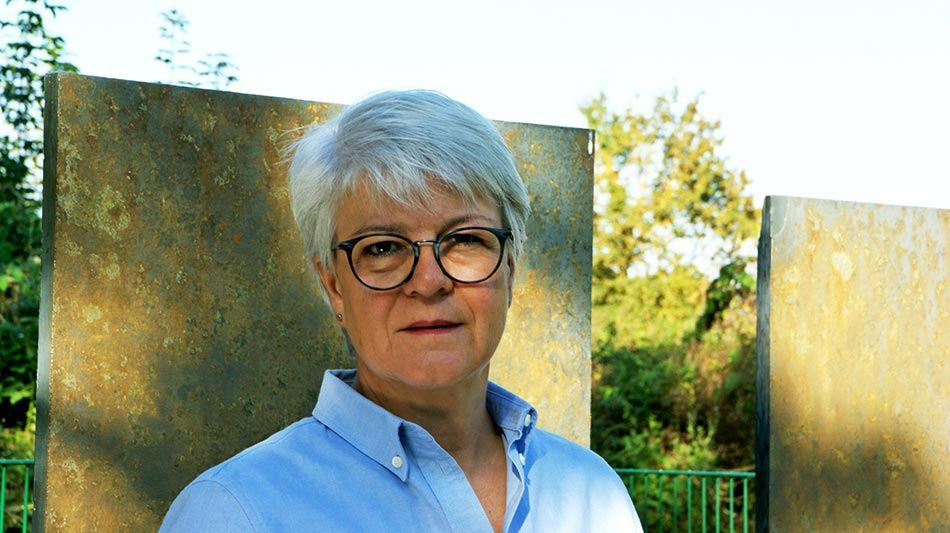 Elke Birkhoelzer Eine Frau mit Brille und blauem Hemd steht vor einer Wand.