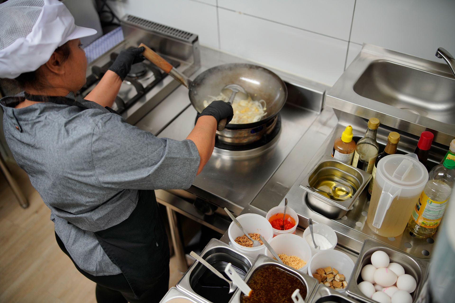 Eine Frau kocht in einer Küche und trägt dabei eine Kochmütze und Handschuhe.