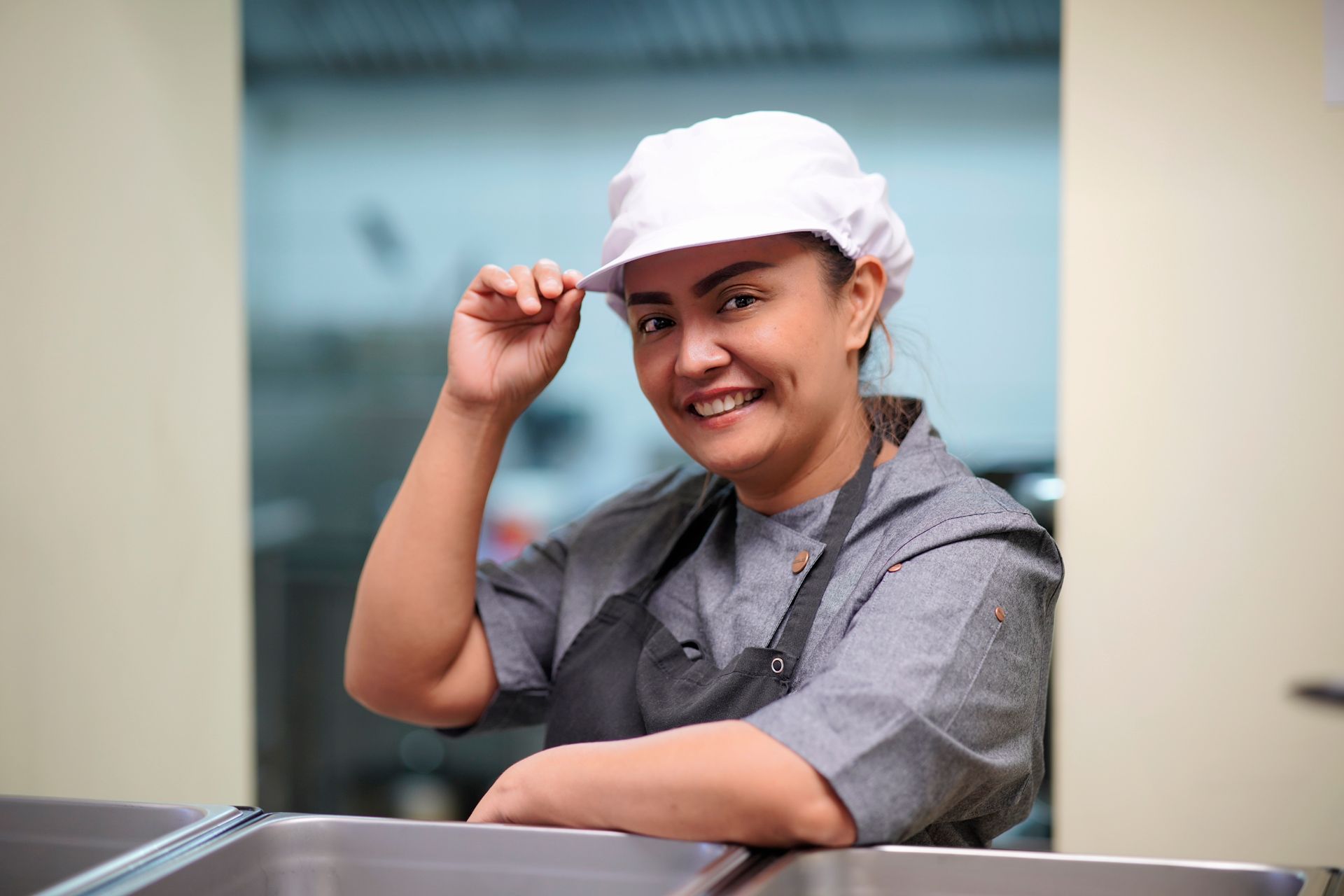 Eine Frau mit weißem Hut und Schürze lächelt in einer Küche.