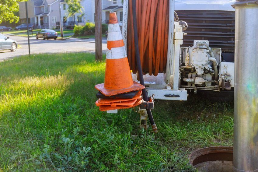 Cono de tráfico naranja en una cuneta cubierta de hierba junto a equipos de servicios públicos y cable enrollado al aire libre.