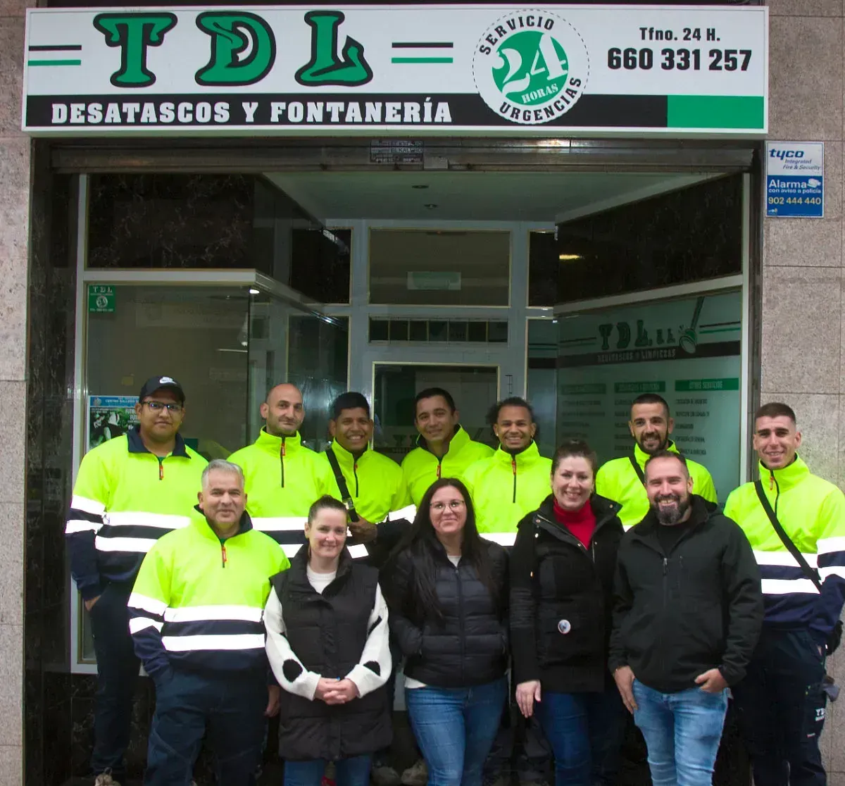 Grupo de empleados posando frente a la tienda de fontanería y construcción TDL, vestidos con chalecos reflectantes.