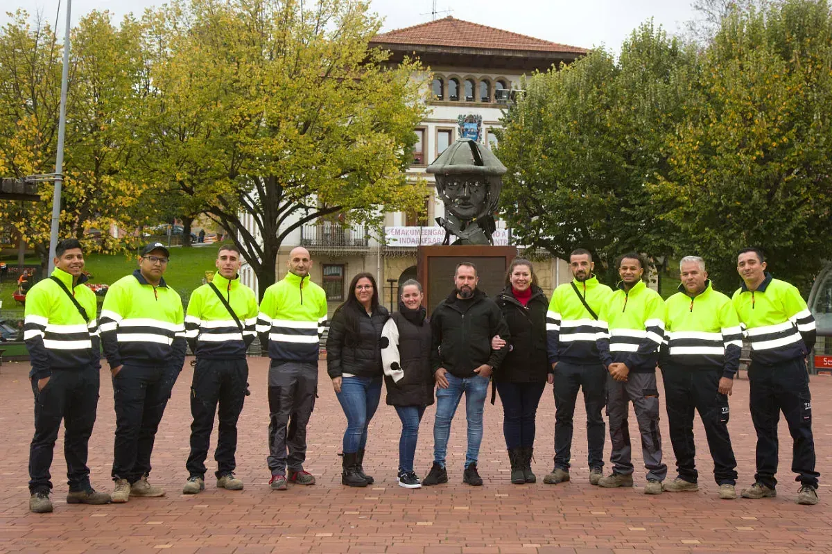 Grupo de personas con chalecos reflectantes de pie en una plaza frente a una fuente y un edificio.