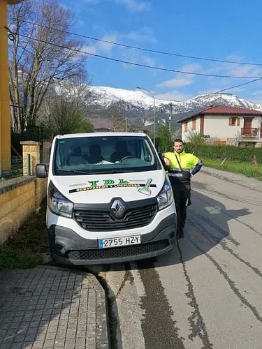 Una furgoneta blanca aparcada al borde de la carretera, con un trabajador con chaleco reflectante de pie junto a ella bajo un soleado paisaje montañoso.