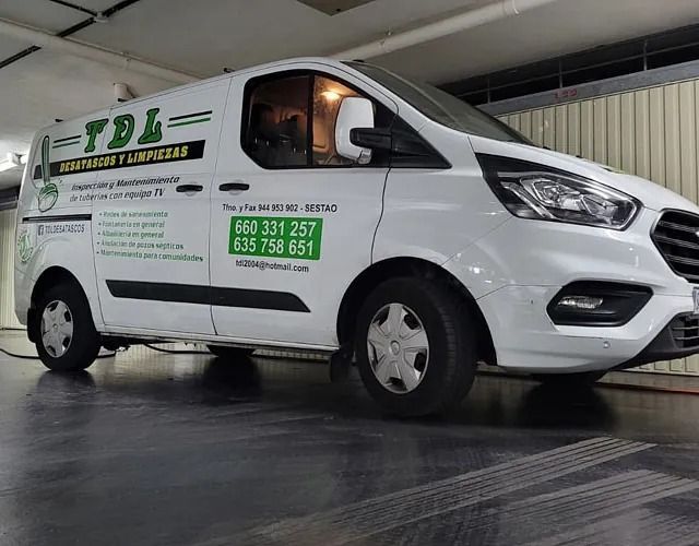 Furgoneta blanca de reparto de muebles TDL aparcada en el interior, con la marca verde y los números de contacto en el lateral.