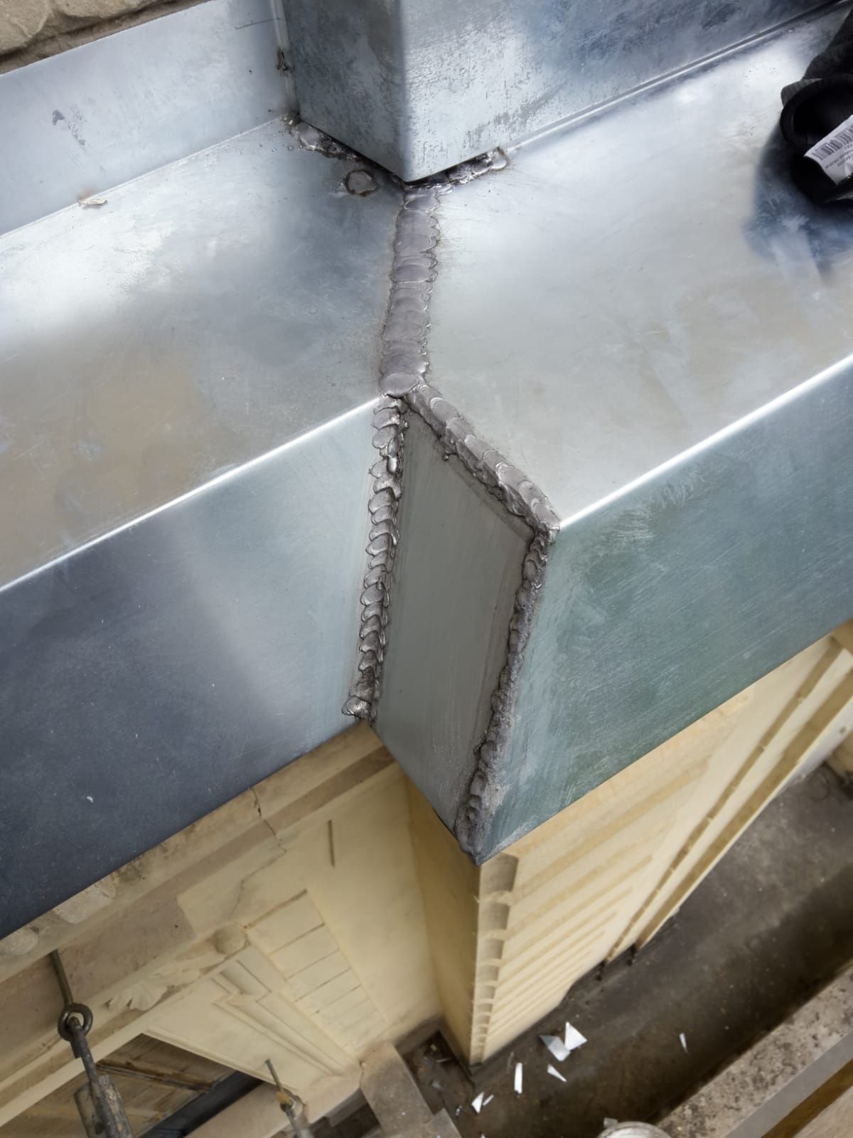 Conduit métallique d'angle avec joints soudés, réfléchissant la lumière.