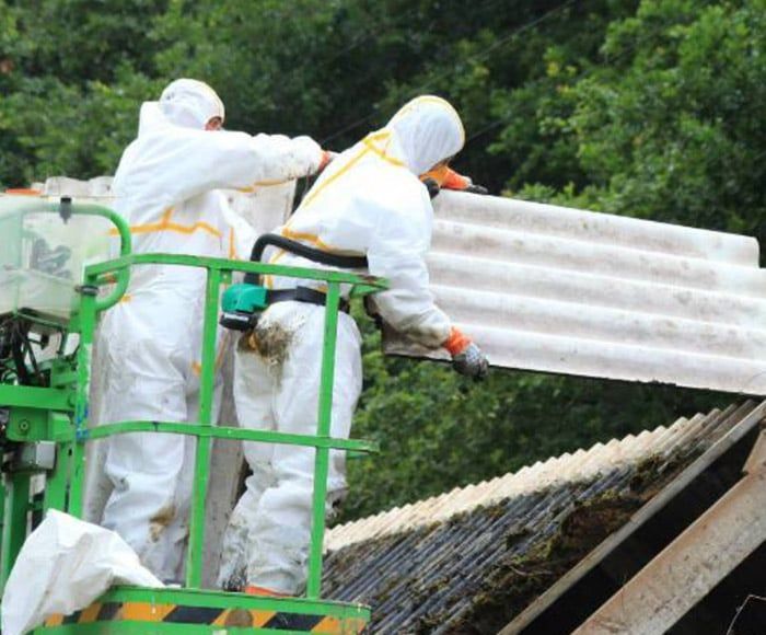 Ouvriers en tenue de protection enlevant une plaque ondulée en amiante d'un toit