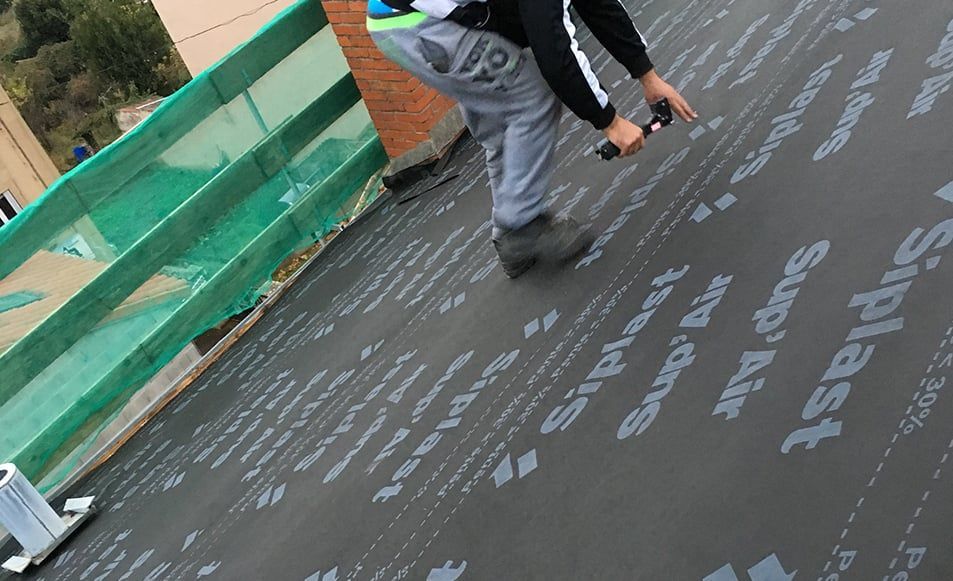 Couvreur installant un matériau de toiture noir, imprimé « Siplast », sur le toit d'un bâtiment.