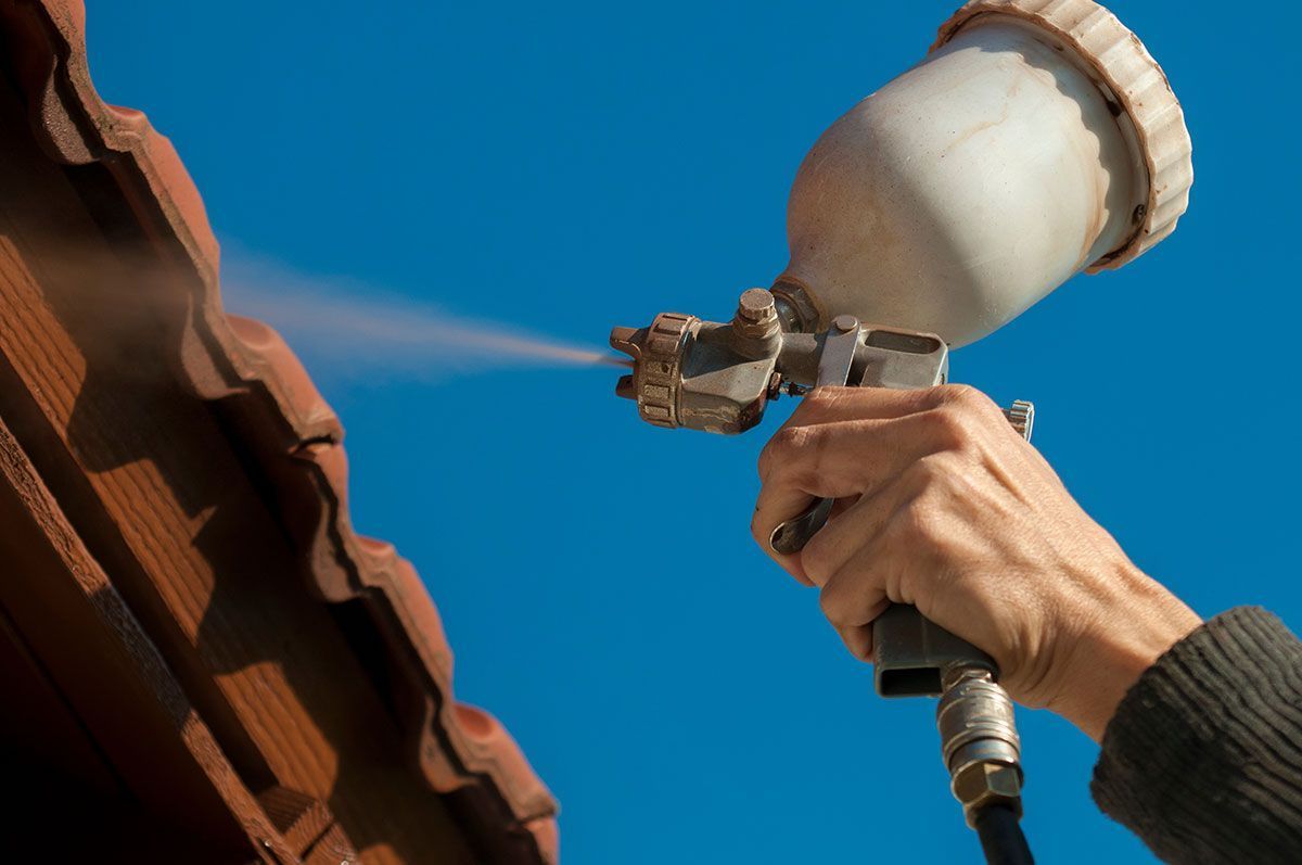 Zoom sur la main d'un homme qui peint des tuiles avec un pistolet à peinture