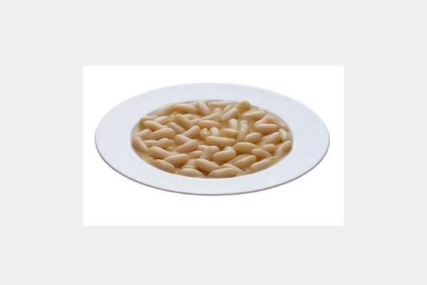 Un plato blanco cubierto con frijoles blancos sobre un fondo blanco.