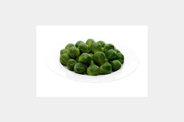 Un plato blanco cubierto con coles de Bruselas verdes sobre un fondo blanco.