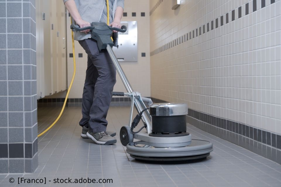 Eine Person bedient eine Bodenpoliermaschine in einem gefliesten Flur.