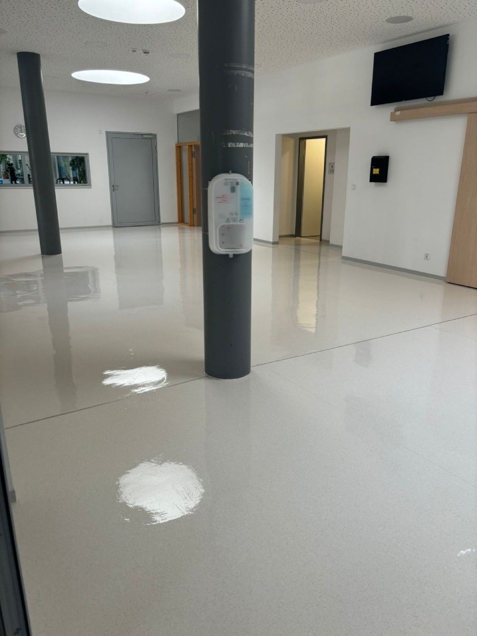 Ein geräumiges Zimmer mit glänzendem Fußboden, einer grauen Säule, weißen Flecken, einer geschlossenen Tür und einem Aufzug.