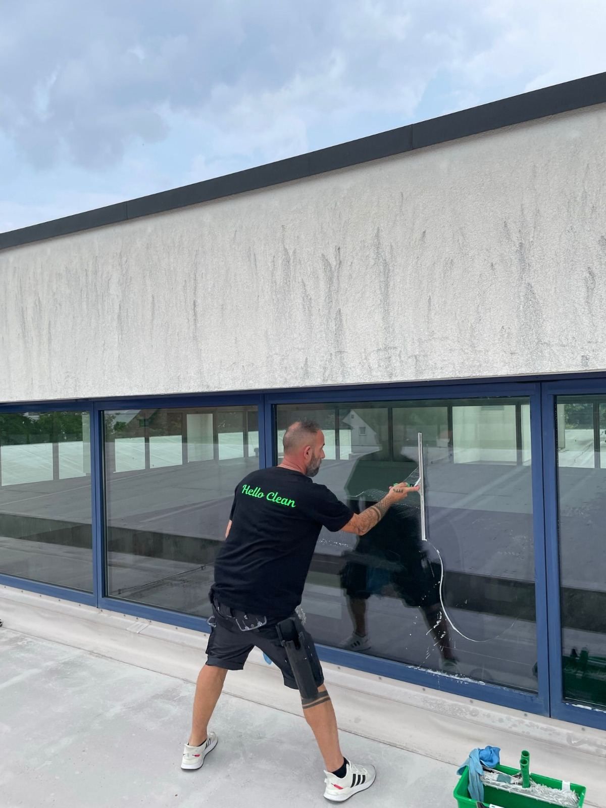 Mann putzt Fenster an einer Hausfassade, bewölkter Himmel.