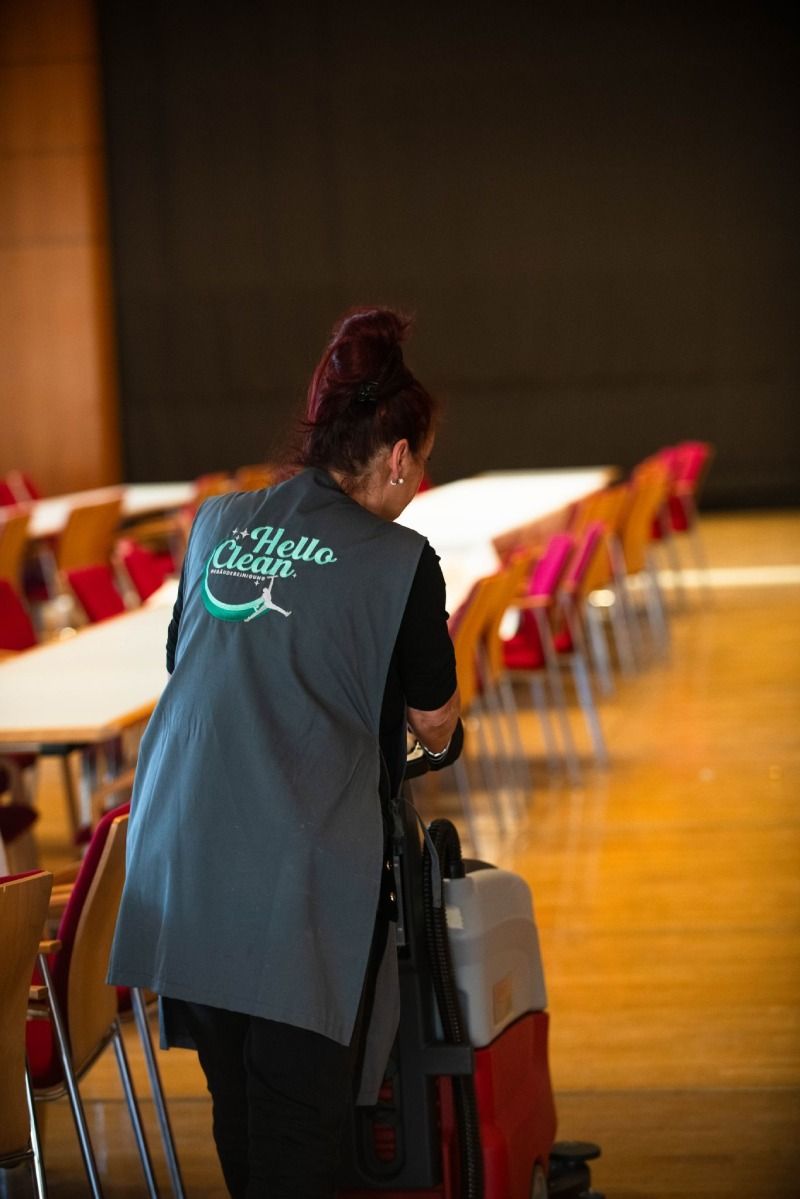 Eine Person saugt einen Büroboden, trägt dabei eine Schürze und Handschuhe.