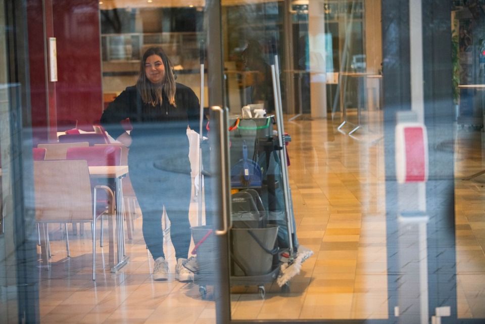 Eine Person steht in einem Gebäude neben einem Reinigungswagen und blickt in die Kamera.