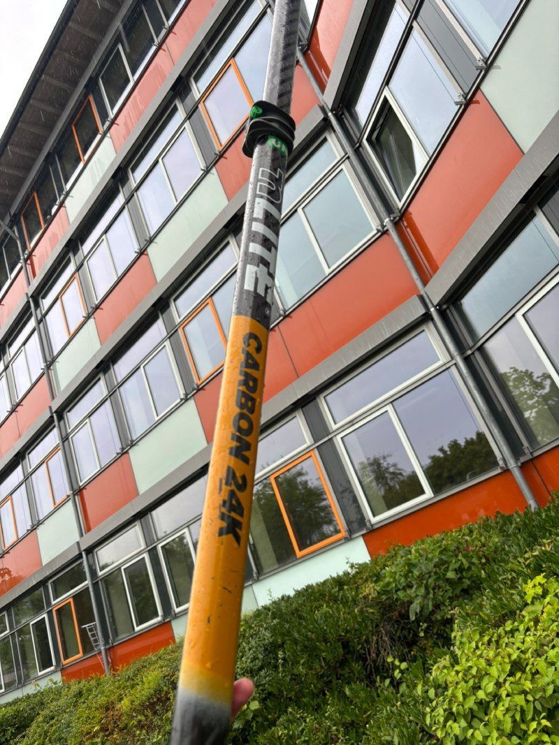 Eine lange Stange aus Kohlefaser zur Fensterreinigung an einem Gebäude mit orange-weißer Fassade.