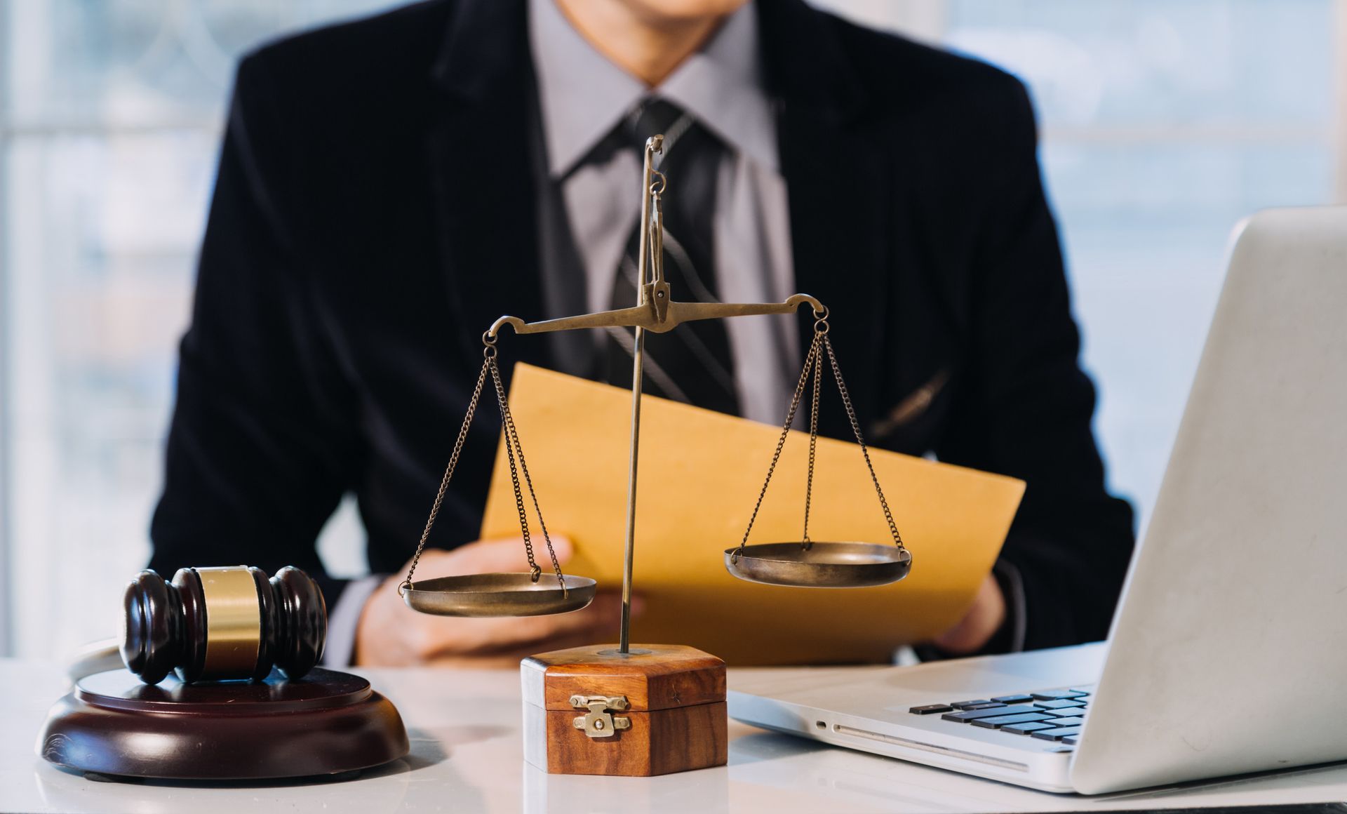 Un hombre está sentado en un escritorio con una computadora portátil y una balanza de justicia.