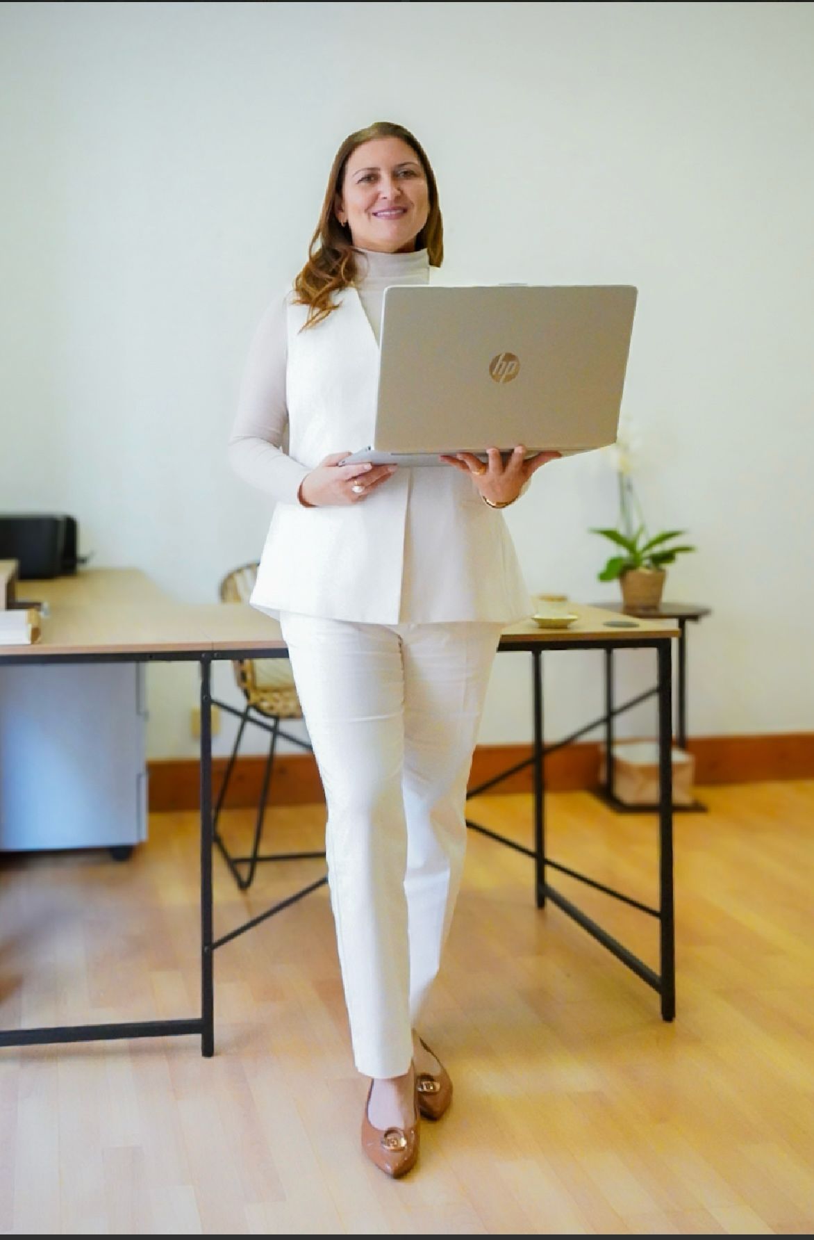 Una mujer con un traje blanco sostiene una computadora portátil HP.