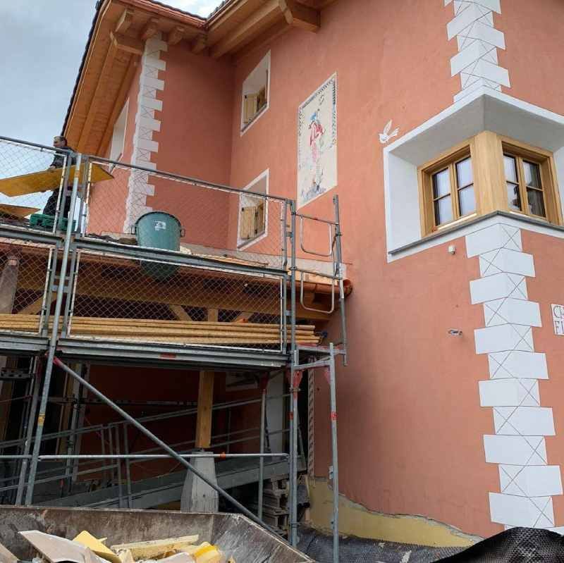 Ein großes orangefarbenes Gebäude mit Gerüst darum herum, Mercuri Gipser & Maler AG