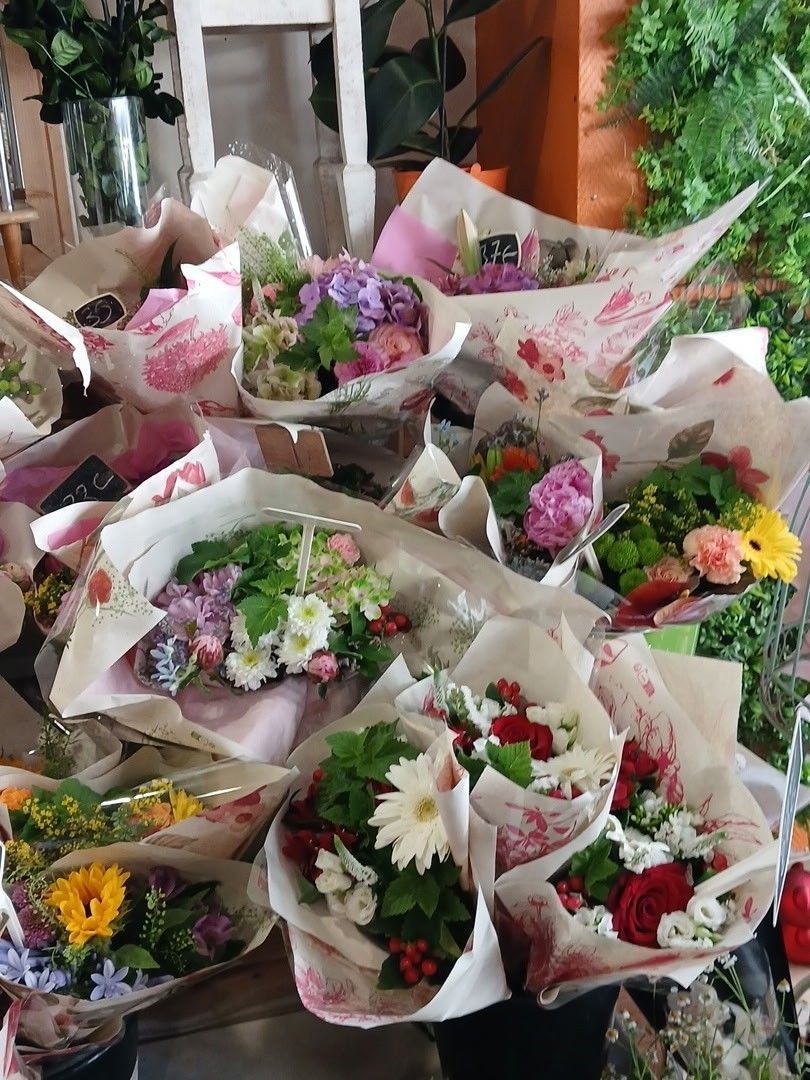 Des bouquets de fleurs colorées assorties, emballés dans du papier blanc, présentés ensemble dans un magasin ou sur un marché.