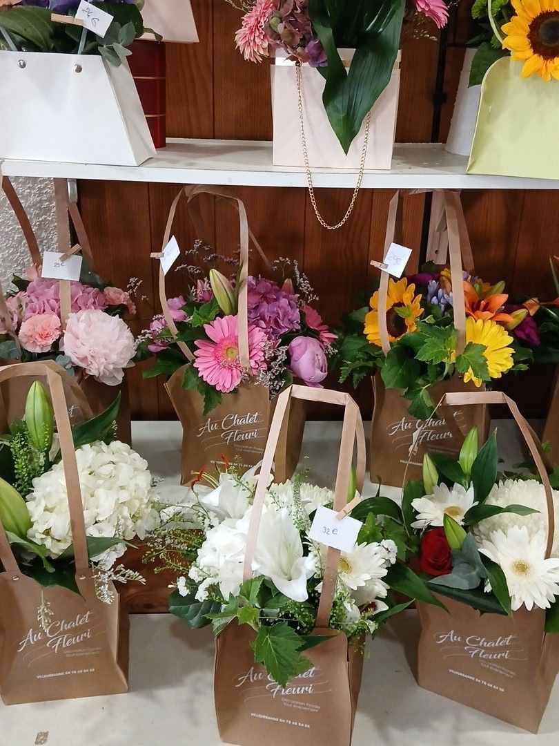 Présentation de bouquets de fleurs roses, blanches, jaunes et orange dans des sacs en papier sur des étagères blanches