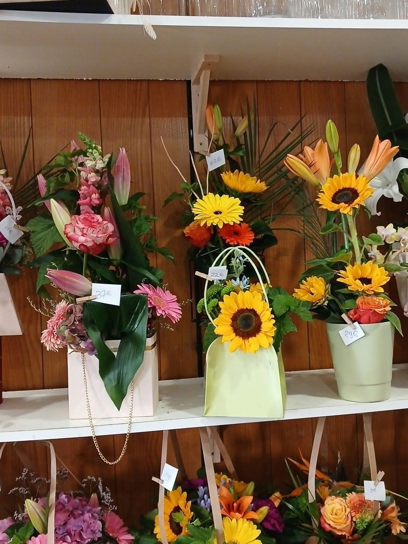 Des compositions de tournesols et de fleurs variées en vase sont présentées sur une étagère dans une vitrine.